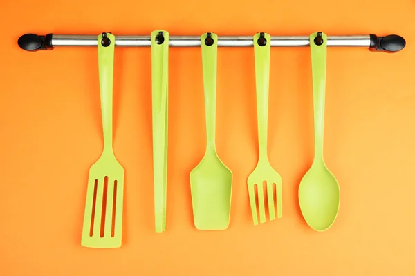 Plastic kitchen utensils on silver hooks on orange background — Stock Photo, Image