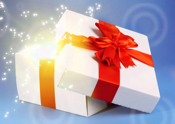 Gift box with bright light on it on blue background — Stock Photo, Image