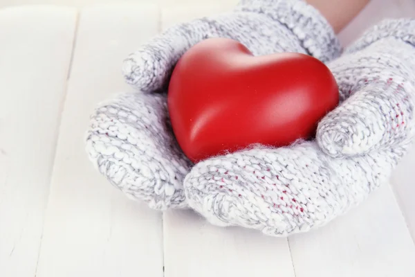 Female hands in mittens with heart on wooden background — Stock Photo, Image