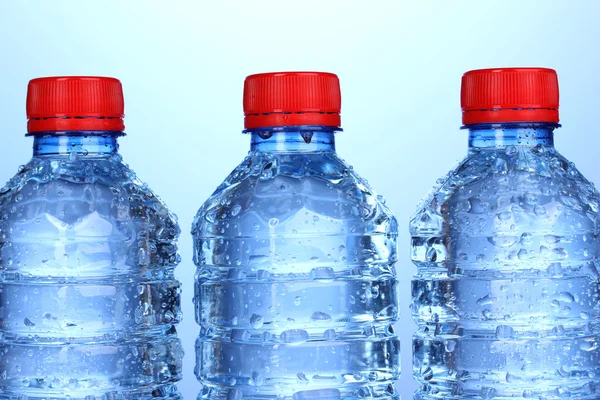 Plastikflaschen mit Wasser auf blauem Hintergrund — Stockfoto