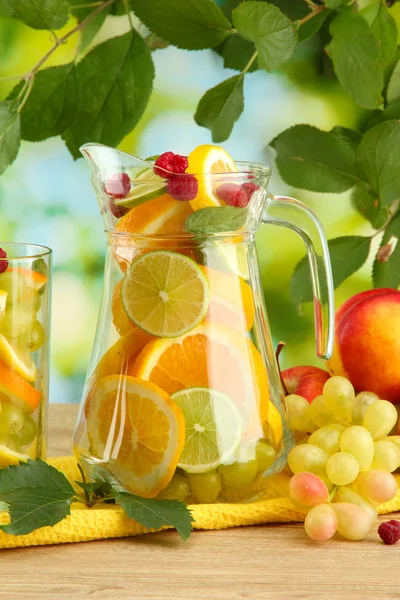 Kruik en glas met citrusvruchten en frambozen, op groene achtergrond — Stockfoto