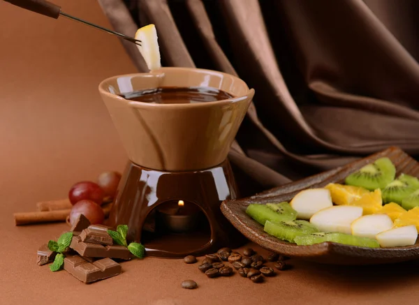 Chocolate fondue with fruits, on brown background — Stock Photo, Image