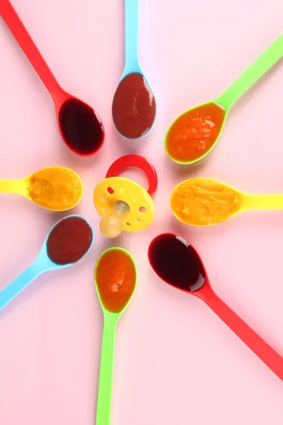Baby puree in spoons with nipple on pink background — Stock Photo, Image