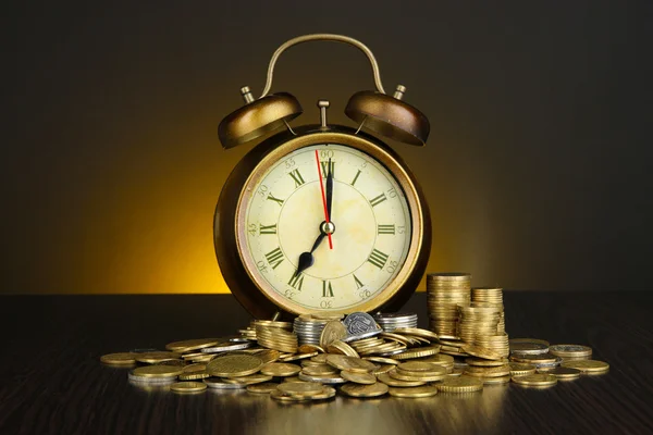 Antieke clock en munten op houten tafel op donkere kleur achtergrond — Stockfoto