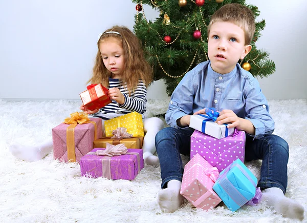 Děti s dárky u vánočního stromu v místnosti — Stock fotografie