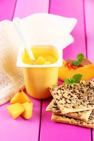 Leckerer Joghurt mit Stücken frischer Früchte, Kekse auf farbigem Holzhintergrund — Stockfoto