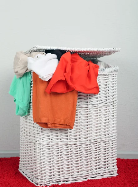 Full laundry basket on color rug on gray wall background — Stock Photo, Image