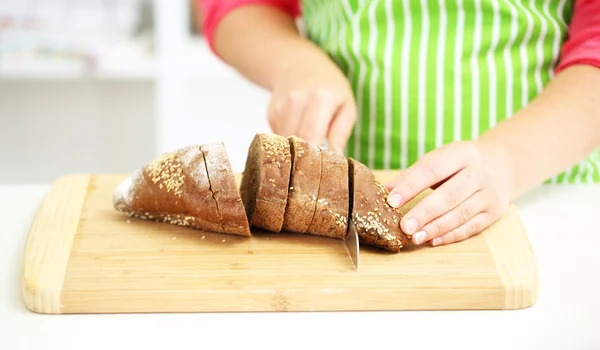 Happy smiling woman in kitchen cutting bread, close-up — Stock Photo, Image