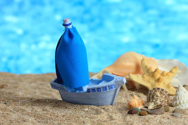 Blue toy ship on sand, on blue background — Stock Photo, Image