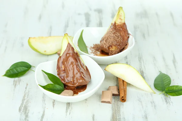 Pear slices in chocolate in bowls on wooden table — Stock Photo, Image