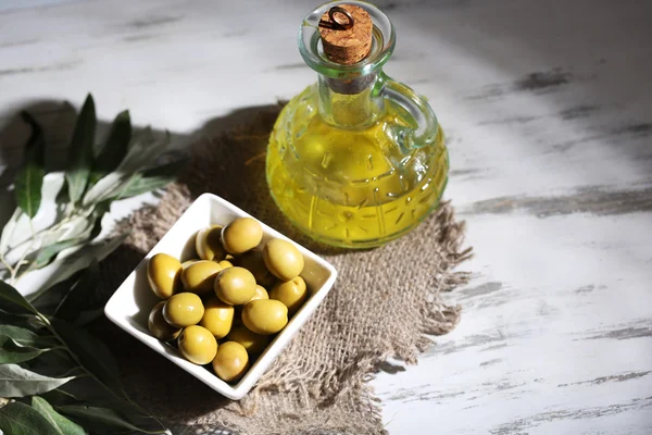 Olijfolie en olijven in kom op rouwgewaad op houten tafel — Stockfoto