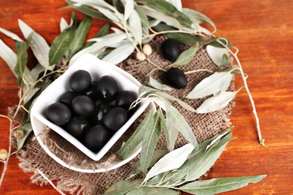 Olive in ciotola con ramo su sacco su tavolo di legno — Foto Stock