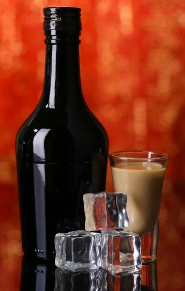 Baileys liqueur in bottle and glass on red background — Stock Photo, Image