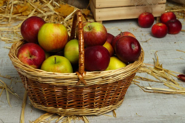 Manzanas en cesta con paja sobre fondo de madera — Foto de Stock