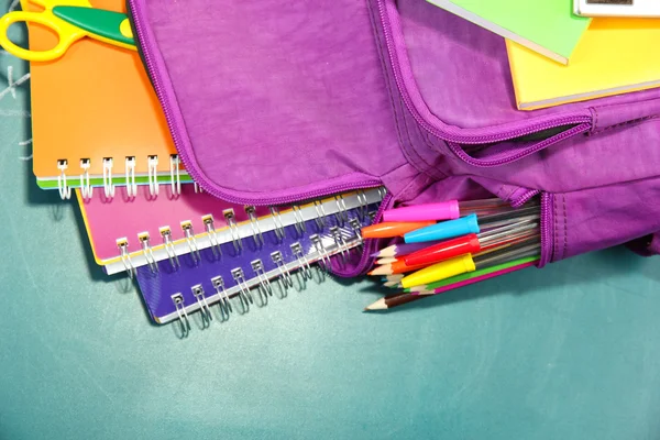 Mochila púrpura con útiles escolares sobre fondo de escritorio verde — Foto de Stock