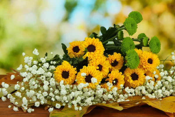 Hermosas flores con hojas amarillas en la mesa sobre fondo brillante — Foto de Stock