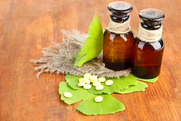 Ginkgo biloba leaves and medicine bottles on wooden background — Stock Photo, Image