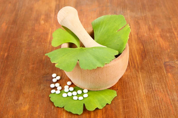 Ginkgo biloba leaves in mortar and pills on wooden background — Stock Photo, Image