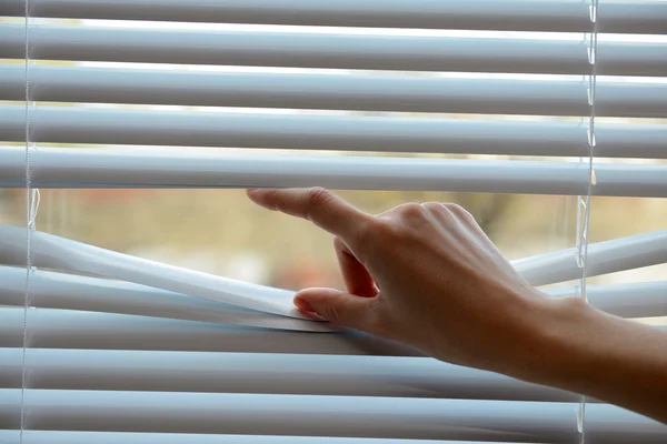 Female hand separating slats of venetian blinds with a finger to see through — Stock Photo, Image