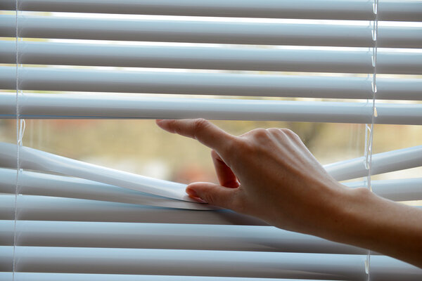 Female hand separating slats of venetian blinds with a finger to see through