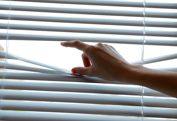 Female hand separating slats of venetian blinds with a finger to see through