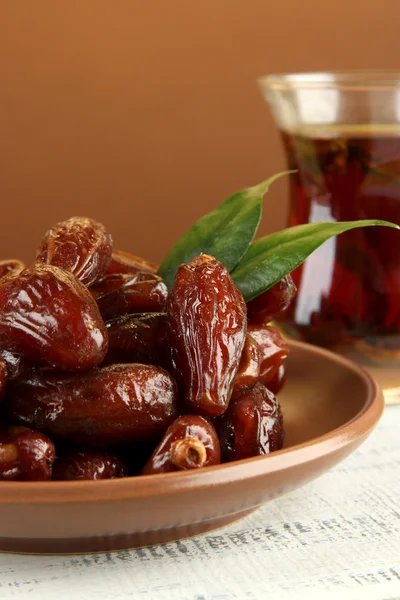 Dried dates on plate with cup of tea on table on brown background