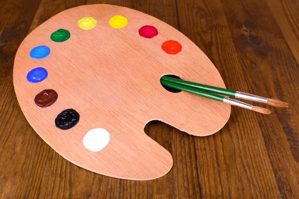 Wooden art palette with paint and brushes on table close-up — Stock Photo, Image