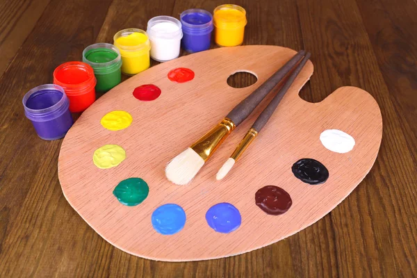 Wooden art palette with paint and brushes on table close-up — Stock Photo, Image