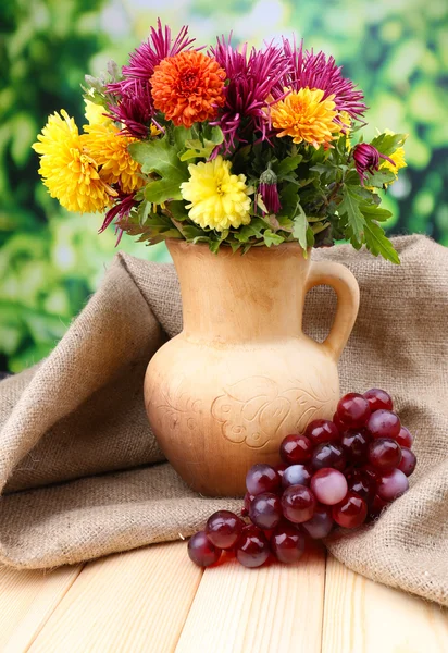 Composition with beautiful flowers in pitcher, and fruits, on bright background — Stock Photo, Image