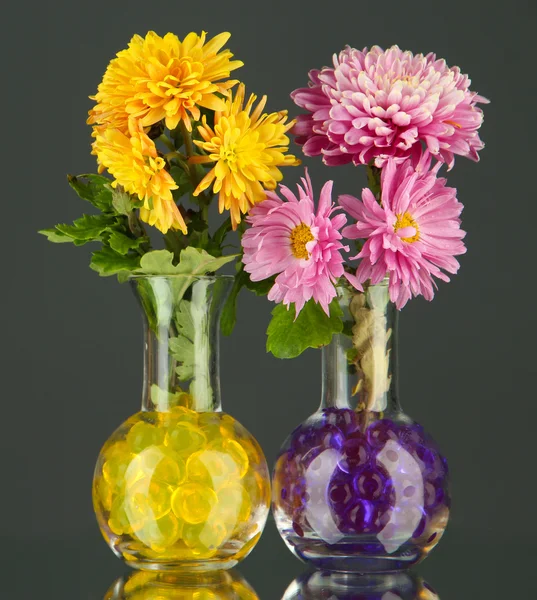Beautiful flowers in vases with hydrogel on table on gray background