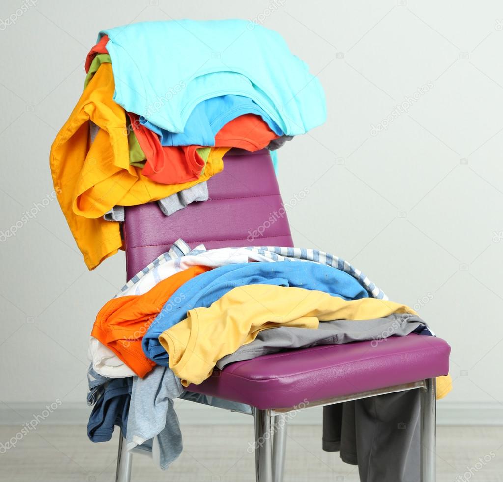 Heap of clothes on color chair, on gray background