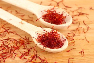 stigmas of saffron in wooden spoons on wooden background close-up clipart