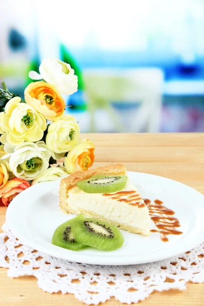 Slice of cheesecake with kiwi fruit on plate, on wooden table, on bright background — Stock Photo, Image