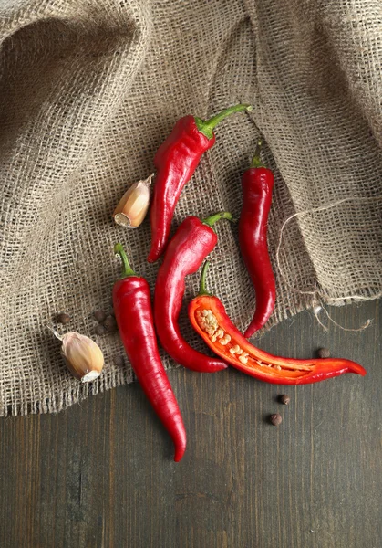 Red hot chili peppers en knoflook, op rouwgewaad, op houten achtergrond — Stockfoto