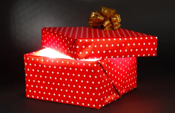 Gift box with bright light on it on dark grey background — Stock Photo, Image