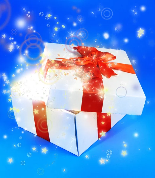 Gift box with bright light on it on blue background — Stock Photo, Image