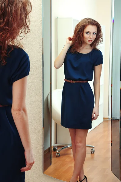 Beautiful girl trying dress near mirror in room — Stock Photo, Image