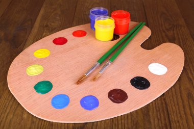 Wooden art palette with paint and brushes on table close-up clipart