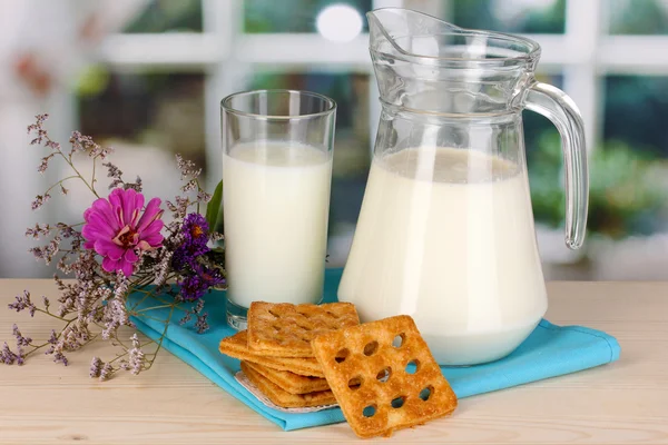 Στάμνα και ποτήρι γάλα με τα cookies για ξύλινο τραπέζι σε φόντο παράθυρο — Φωτογραφία Αρχείου