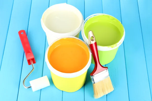 Conjunto para pintura: vasos de pintura, pincéis, rolo de pintura sobre mesa de madeira azul — Fotografia de Stock