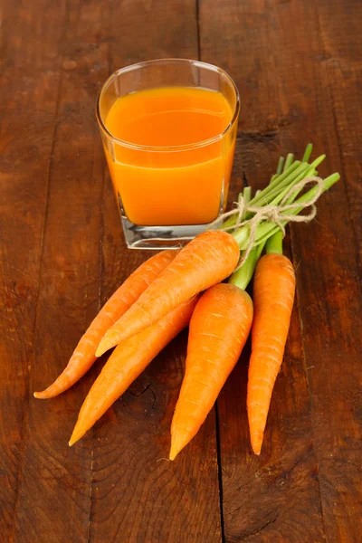 Heap of carrots, glass of juice, on wooden background — Stock Photo, Image