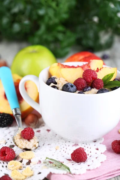 Oatmeal in cup with berries on napkins on wooden table on plant background — Stock Photo, Image