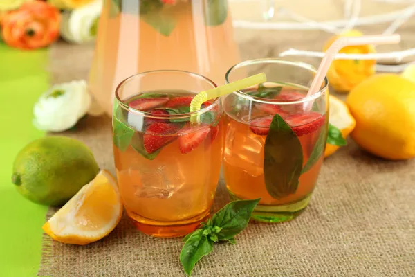 Basil lemonade with strawberry in jug and glass, on wooden table, on bright background — Stock Photo, Image