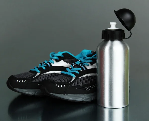 Botella deportiva y zapatillas de deporte sobre fondo gris —  Fotos de Stock