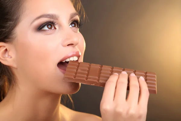 Portrait of beautiful young girl with chocolate on brown background — Stock Photo, Image