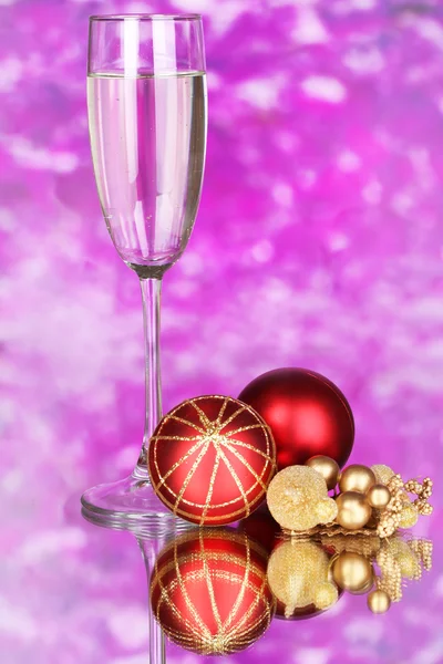 Glass of champagne and Christmas balls on purple background — Stock Photo, Image