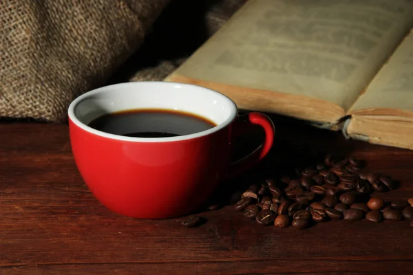 Kopp kaffe med kaffebönor och bok om träbord på säckväv bakgrund — Stockfoto