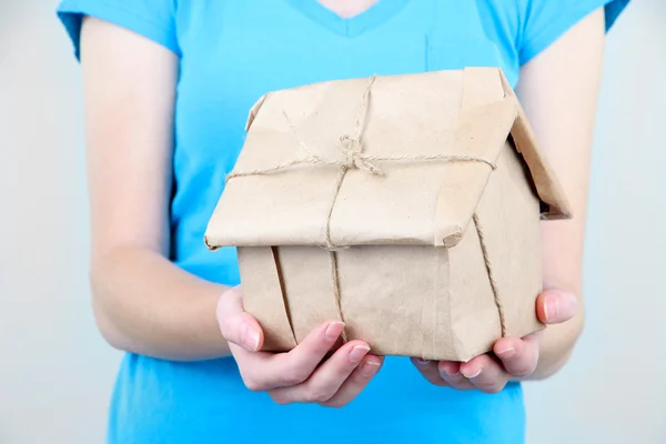 Manos de mujer sosteniendo una casa envuelta en papel kraft marrón — Foto de Stock