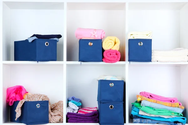 Blauwe textiel vakken met handdoeken en kleren in witte planken — Stockfoto