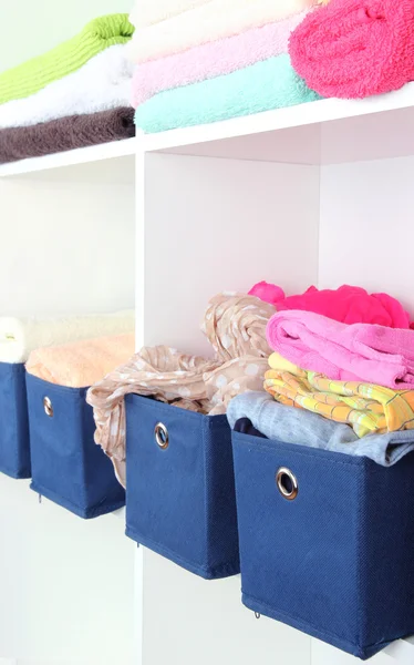 Blue textile boxes with towels and clothes in white shelves — Stock Photo, Image